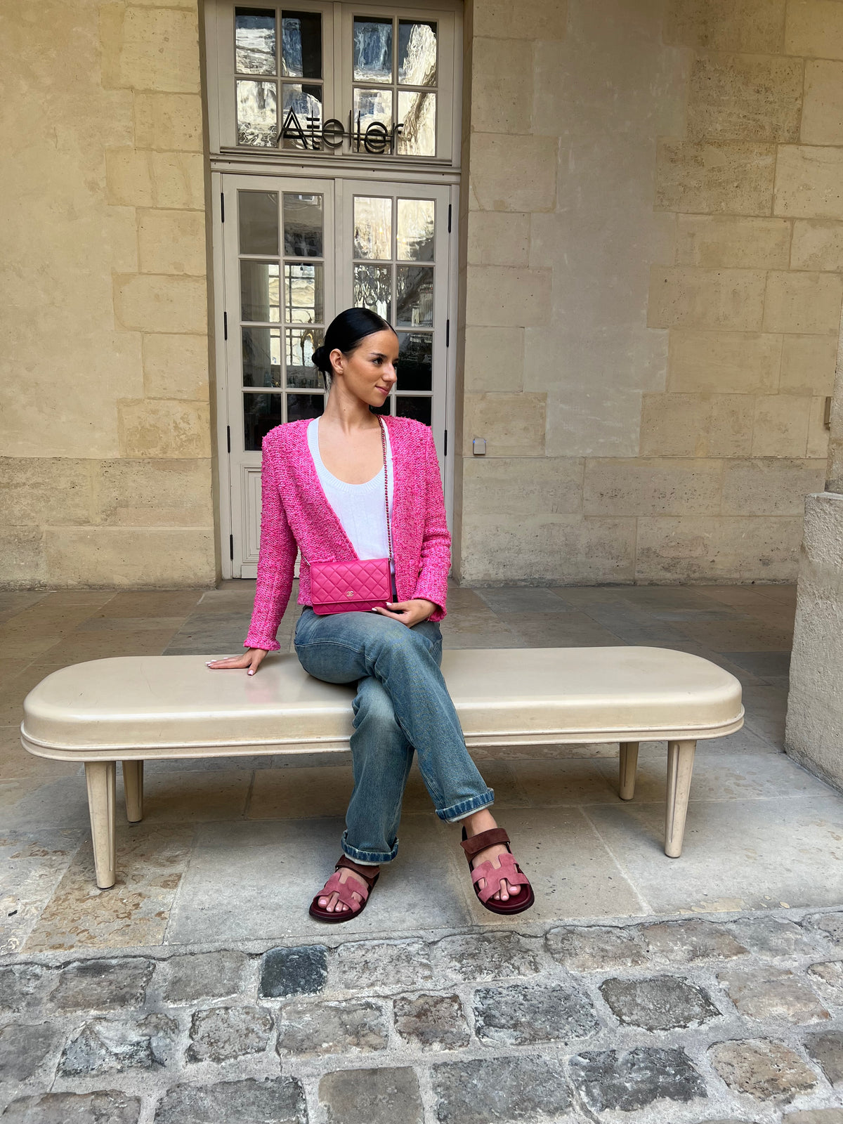 Sac Chanel rose matelassé porté en bandoulière, avec une veste rose devant une façade en pierre.